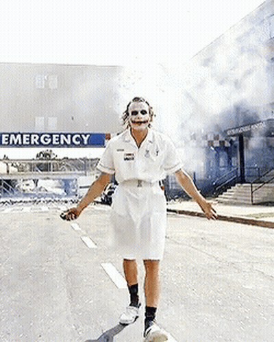 A Man In A Nurse Costume Is Walking Down A Street In Front Of An Emergency Sign GIF