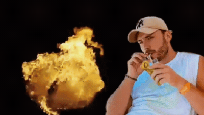 A Man In A Ny Hat Is Drinking Through A Straw In Front Of A Fireball . GIF