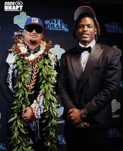 A Man In A Ny Hat Stands Next To A Man In A Suit GIF
