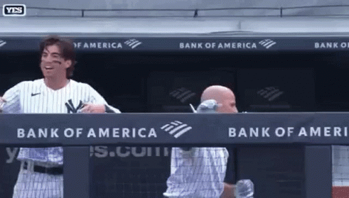 A Man In A Ny Yankees Uniform Stands In A Dugout With A Bank Of America Banner Behind Him GIF