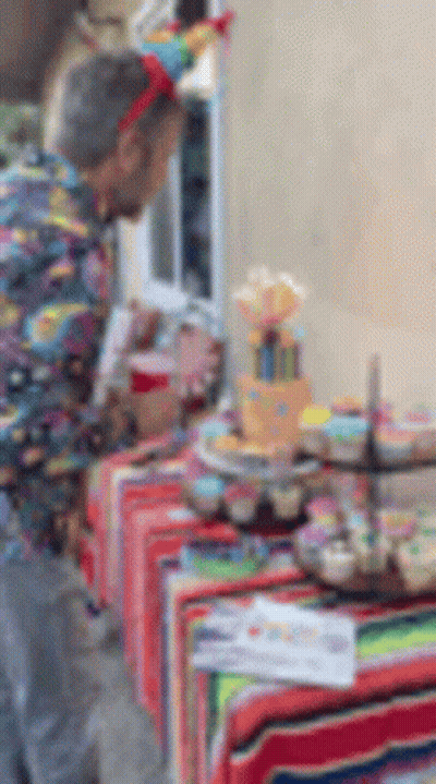 A Man In A Party Hat Is Standing In Front Of A Table With Cupcakes On It . GIF