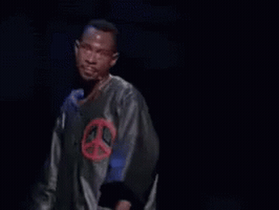 A Man In A Peace Sign Shirt Is Standing In Front Of A Microphone With The Words Next Time Above Him GIF