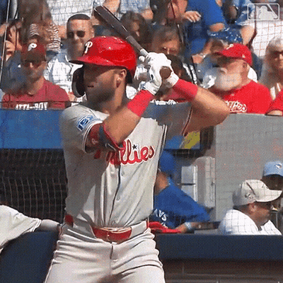 A Man In A Phillies Uniform Is Swinging At A Baseball GIF