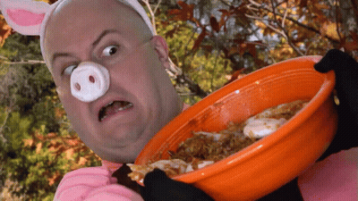 A Man In A Pig Costume Is Holding An Orange Bowl Of Food GIF