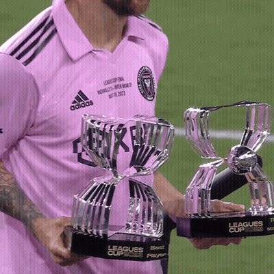 A Man In A Pink Adidas Shirt Is Holding Two League Cup Trophies GIF
