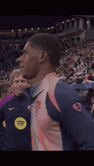 A Man In A Pink And Blue Jersey Is Standing In Front Of A Crowd Of People . GIF