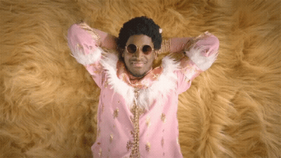 A Man In A Pink And Gold Outfit Is Laying On A Furry Rug GIF