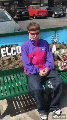 A Man In A Pink And Purple Jacket Is Sitting On A Bench In Front Of A Wall That Says Elco GIF