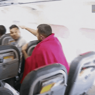 A Man In A Pink Blanket Is Sitting In A Plane GIF