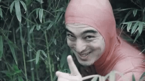A Man In A Pink Bodysuit Is Giving A Thumbs Up While Standing In A Forest . GIF