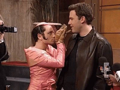 A Man In A Pink Dress Is Kissing Another Man On The Cheek GIF