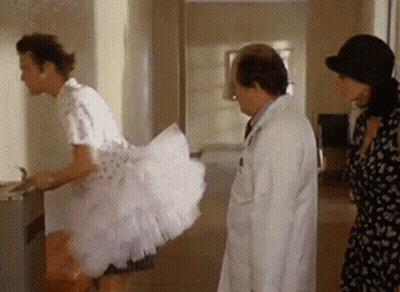 A Man In A Pink Dress Is Standing Next To A Doctor And A Woman In A Hat . GIF