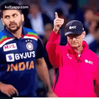 A Man In A Pink Jacket Is Giving A Thumbs Up While A Man In A Blue Shirt Is Standing Behind Him . GIF