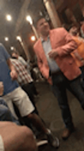 A Man In A Pink Jacket Is Standing In A Crowd Of People At A Party . GIF