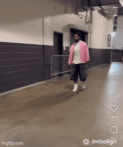 A Man In A Pink Jacket Is Walking Down A Hallway With Invisalign GIF