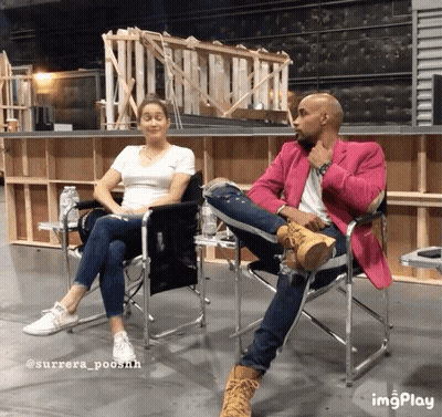 A Man In A Pink Jacket Sits Next To A Woman In A White Shirt And Jeans GIF