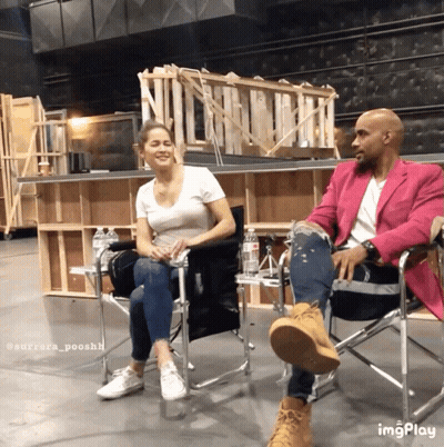A Man In A Pink Jacket Sits Next To A Woman In Chairs GIF