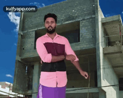 A Man In A Pink Shirt And Purple Shorts Is Standing In Front Of A Building Under Construction GIF