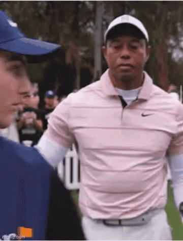 A Man In A Pink Shirt And White Pants Is Standing Next To A Man In A Blue Hat On A Golf Course . GIF