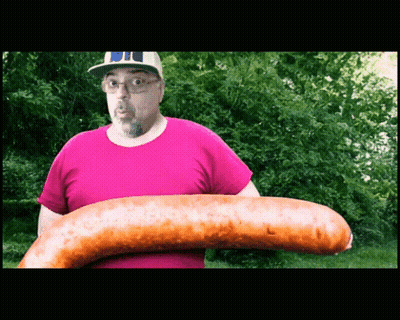 A Man In A Pink Shirt Holds A Very Large Sausage GIF