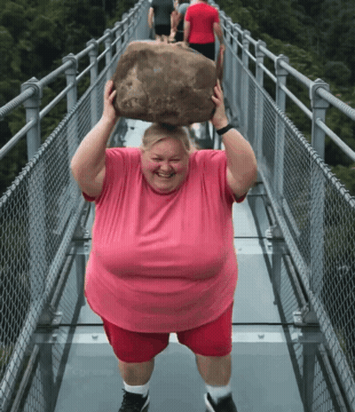 A Man In A Pink Shirt Is Carrying A Large Rock Over His Head GIF