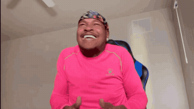 A Man In A Pink Shirt Is Holding A Game Controller And Laughing GIF