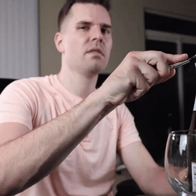 A Man In A Pink Shirt Is Holding A Pair Of Tweezers Over A Bottle GIF