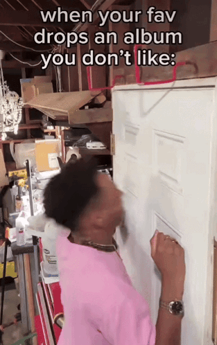 A Man In A Pink Shirt Is Knocking On A Door In A Garage GIF