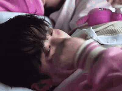 A Man In A Pink Shirt Is Laying In Bed With A Pink Stuffed Animal . GIF