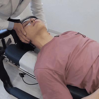 A Man In A Pink Shirt Is Laying On A Table Getting A Massage GIF