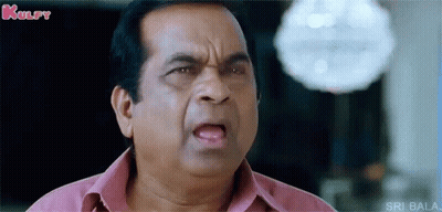 A Man In A Pink Shirt Is Making A Funny Face And Looking At The Camera . GIF