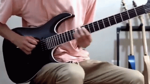 A Man In A Pink Shirt Is Playing A Black Guitar GIF