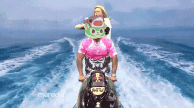 A Man In A Pink Shirt Is Riding A Jet Ski With A Woman In A Shark Mask Behind Him GIF