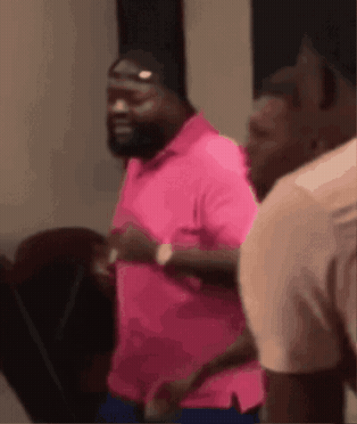 A Man In A Pink Shirt Is Running On A Treadmill With Other Men . GIF