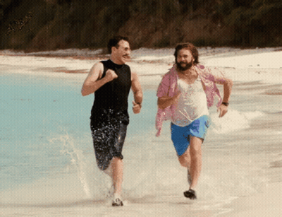 A Man In A Pink Shirt Is Running On The Beach With Another Man GIF