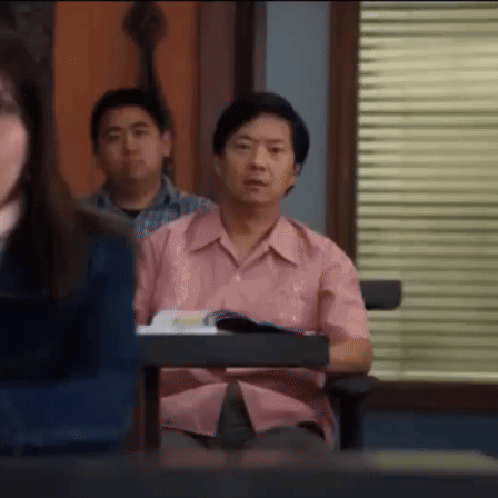A Man In A Pink Shirt Is Sitting At A Desk In A Classroom With Other Students . GIF
