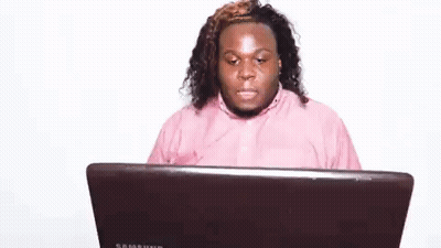 A Man In A Pink Shirt Is Sitting At A Laptop Computer . GIF