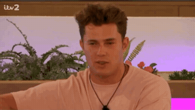 A Man In A Pink Shirt Is Sitting In Front Of A Pink Wall With Plants . GIF
