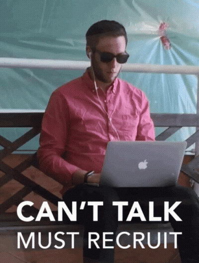 A Man In A Pink Shirt Is Sitting On A Bench Using An Apple Laptop With The Words " Can 'T Talk Must Recruit " Above Him GIF