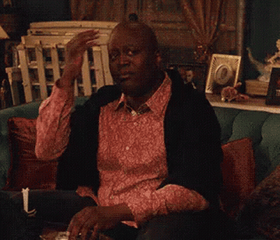 A Man In A Pink Shirt Is Sitting On A Couch Drinking A Glass Of Wine . GIF