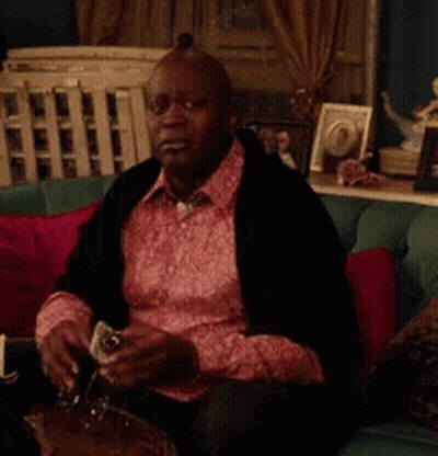 A Man In A Pink Shirt Is Sitting On A Couch GIF