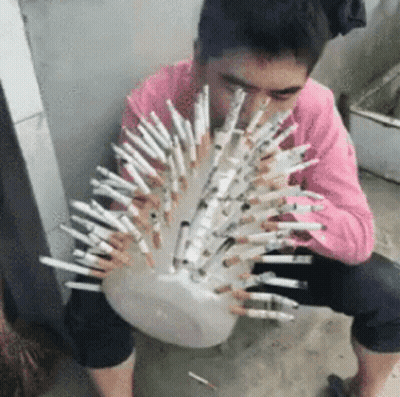 A Man In A Pink Shirt Is Sitting On The Ground Holding A Bowl Of Cigarettes . GIF