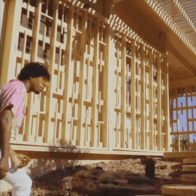 A Man In A Pink Shirt Is Standing In Front Of A Building That Is Being Built GIF