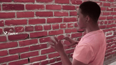 A Man In A Pink Shirt Is Standing In Front Of A Red Brick Wall . GIF