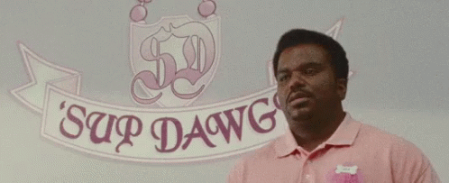 A Man In A Pink Shirt Is Standing In Front Of A Sign That Says Sup Dawg Dawg . GIF