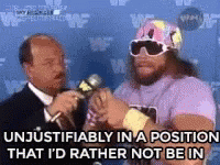 A Man In A Pink Shirt Is Talking Into A Microphone While A Man In A Suit Looks On . GIF