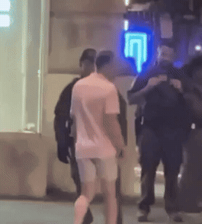A Man In A Pink Shirt Is Walking In Front Of A Blue Sign That Says ' U ' On It . GIF