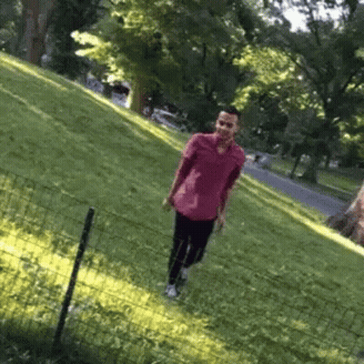 A Man In A Pink Shirt Is Walking Through A Grassy Field GIF