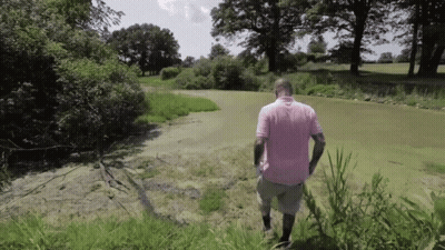 A Man In A Pink Shirt Is Walking Through A Grassy Field GIF