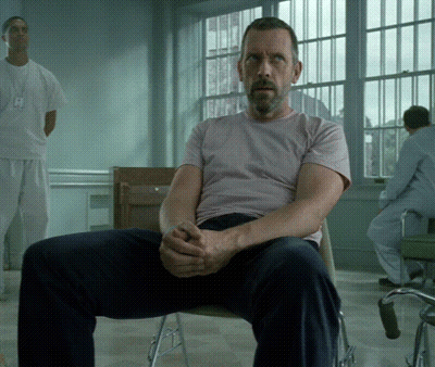 A Man In A Pink Shirt Sits In A Chair With His Hands Folded GIF